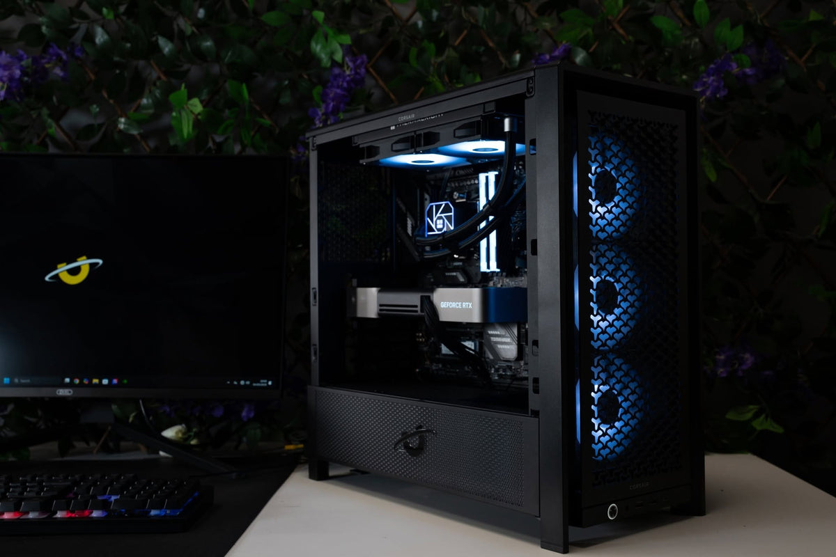 Ballista gaming PC on a desk, showing its full size chassis, internal components and front cooling fans illuminated in blue.